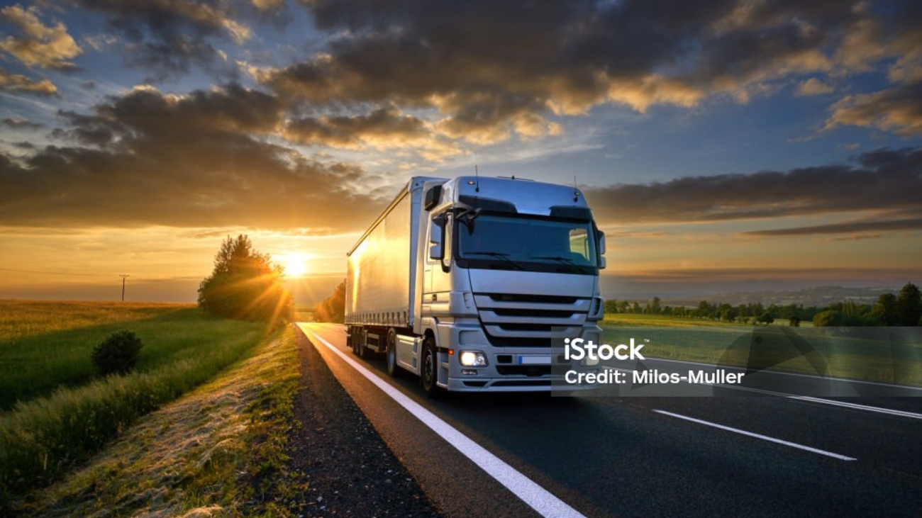 Truck driving on the asphalt road in rural landscape at sunset with dark clouds