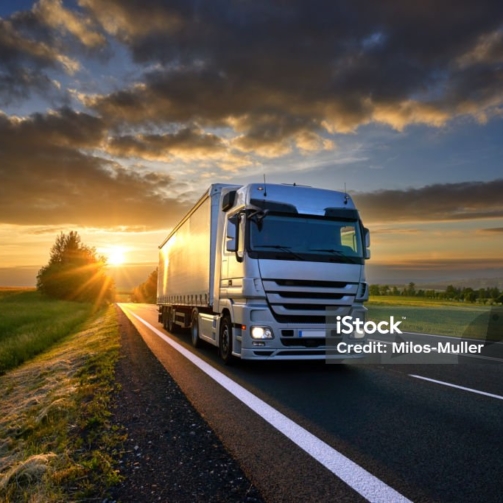 Truck driving on the asphalt road in rural landscape at sunset with dark clouds