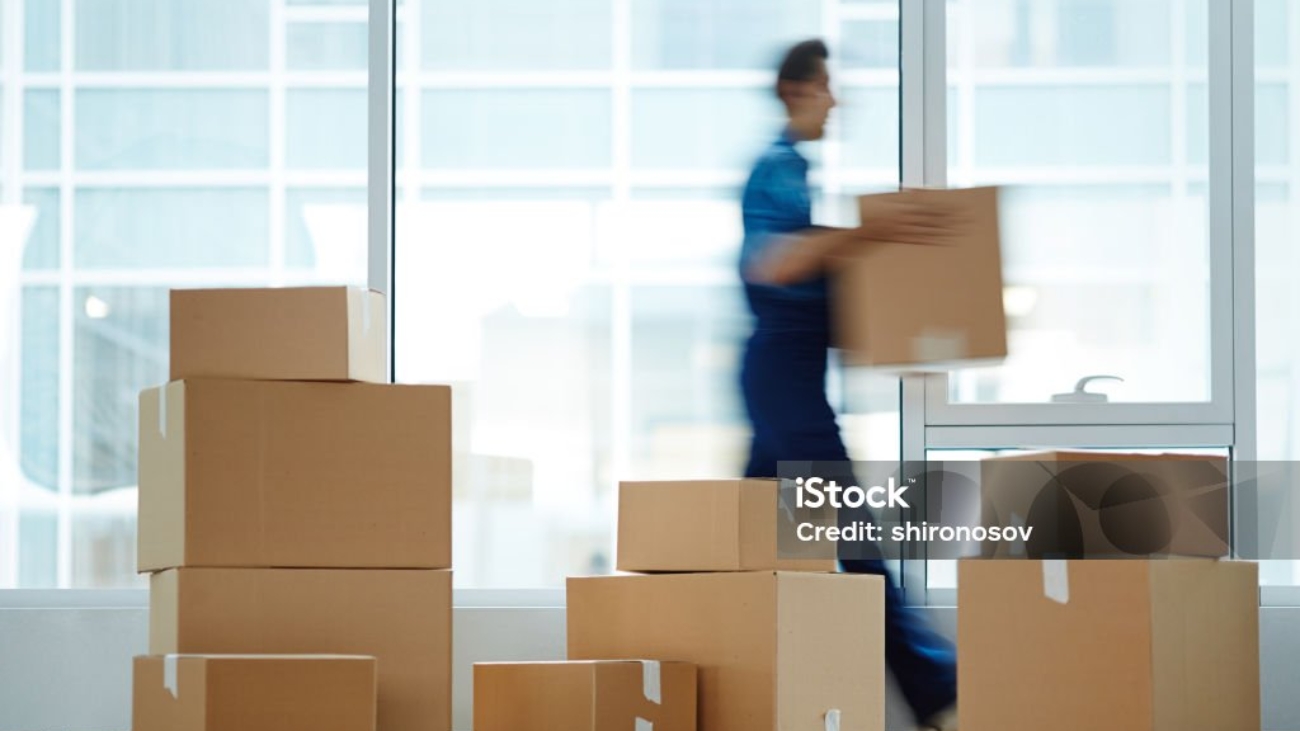 Blurred motion of contemporary worker with packed box walking to new office while delivering it to client