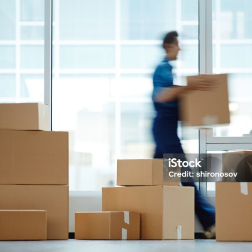 Blurred motion of contemporary worker with packed box walking to new office while delivering it to client